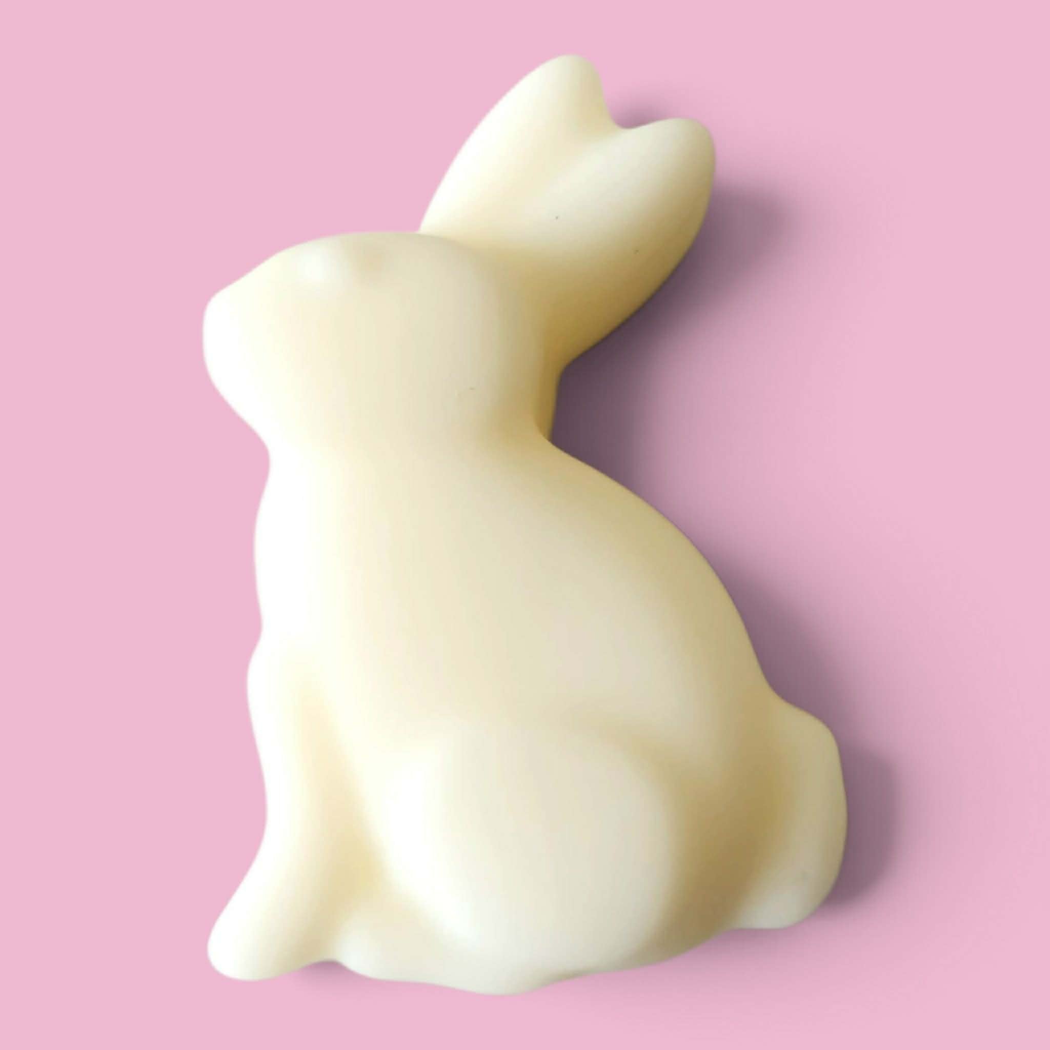 A smooth, matte off-white bunny-shaped object, soy wax melt, shown against a solid pink background.