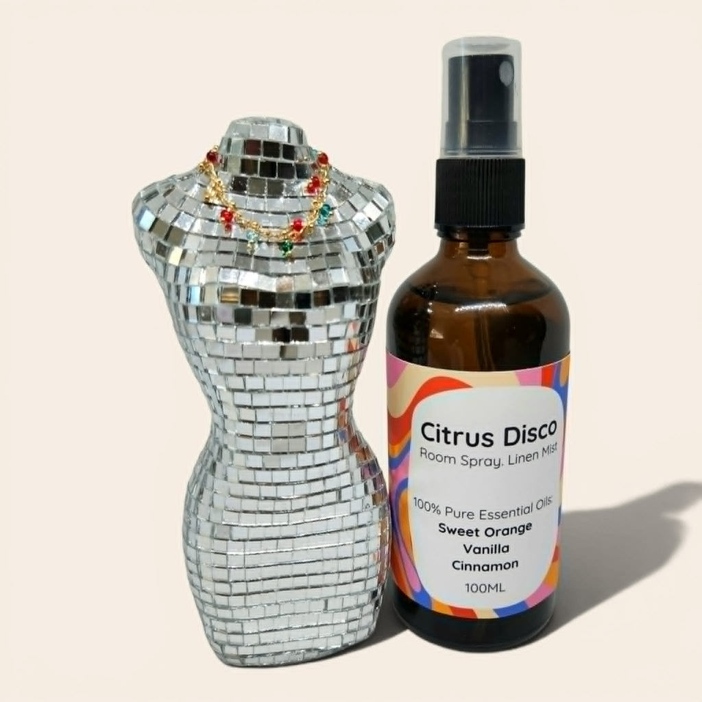 Bottle of Citrus Disco room spray next to a disco ball on a beige background