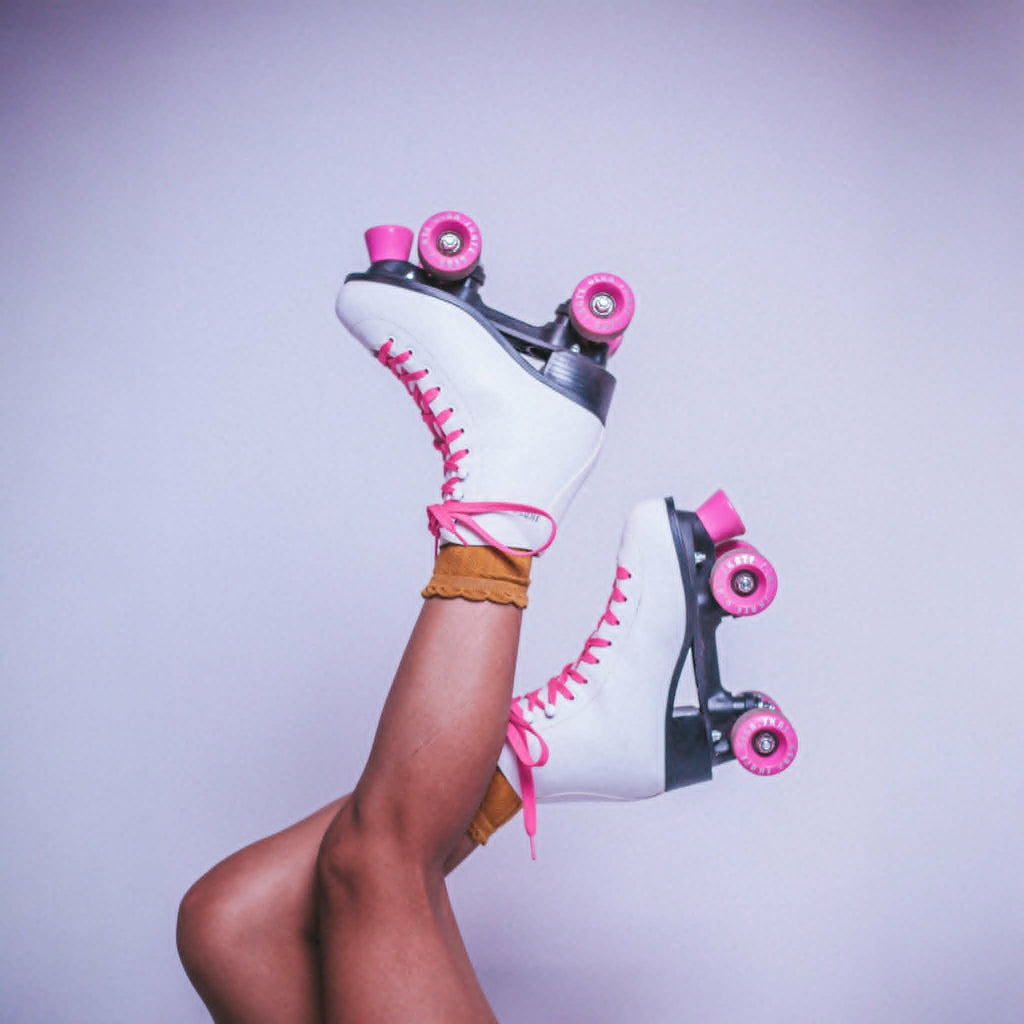 White roller skates with pink wheels held by a person against a light purple background