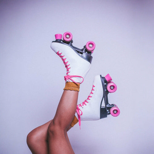 White roller skates with pink wheels held by a person against a light purple background
