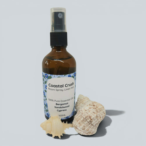Bottle of 'Coastal Crush' room spray with a shell on a light gray background