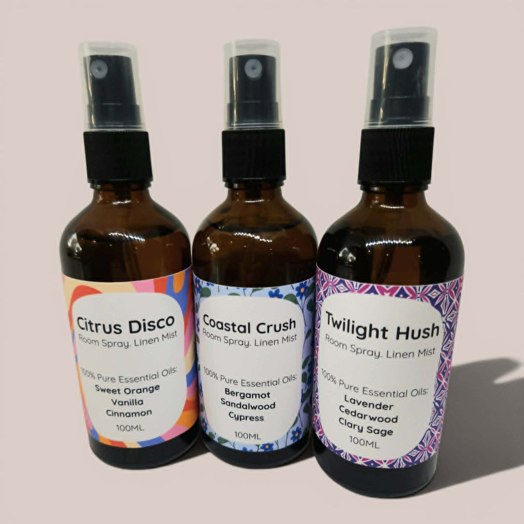 Three brown spray bottles with colorful labels on a light pink background
