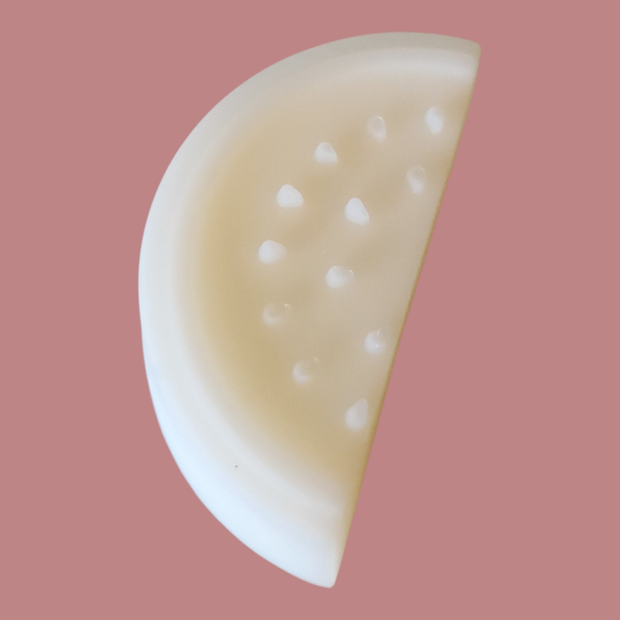 Half of a white melon with small holes on a pink background