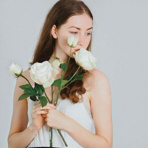 Pretty young woman posing with white roses in a white dress