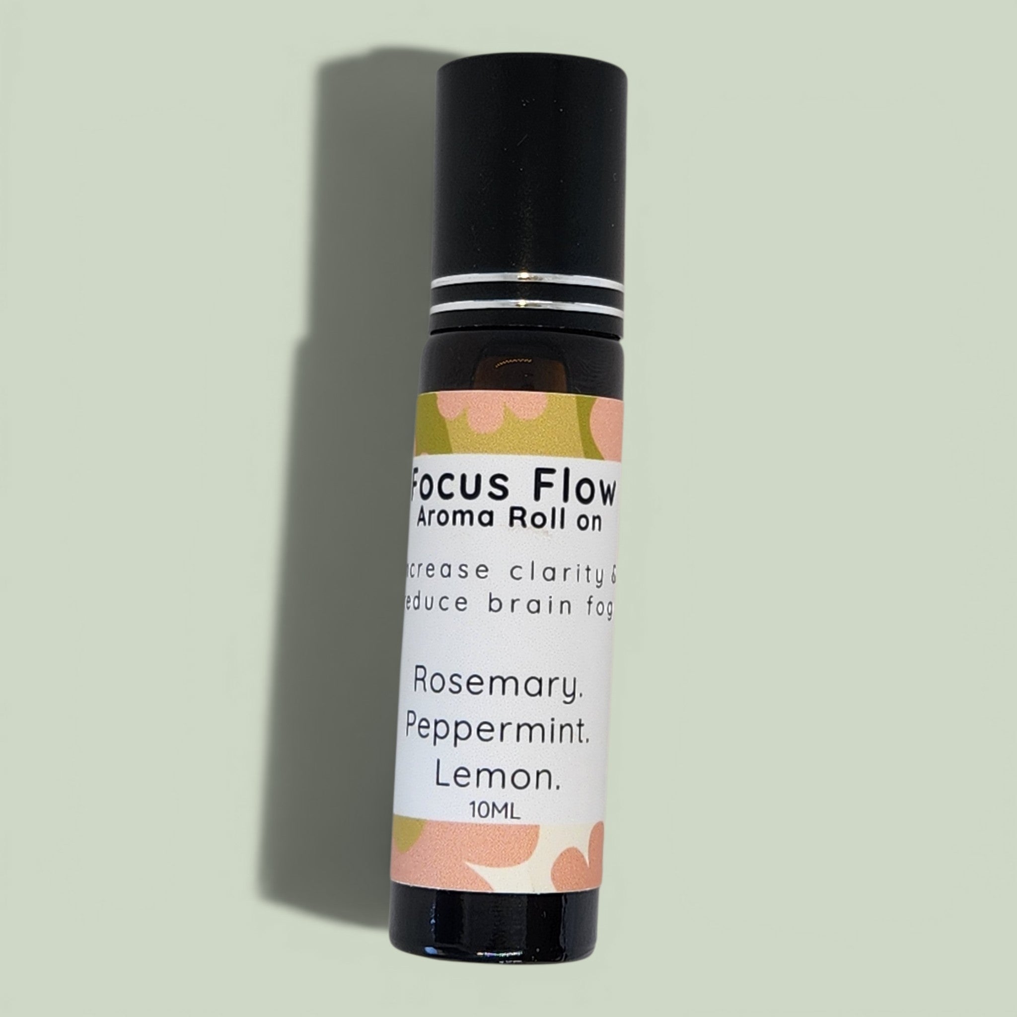 A 10ml roll-on bottle of Focus Flow Aroma Roll on by Calm Down Studio, featuring a black cap and a white label with peach and green floral accents, set against a solid sage green background.