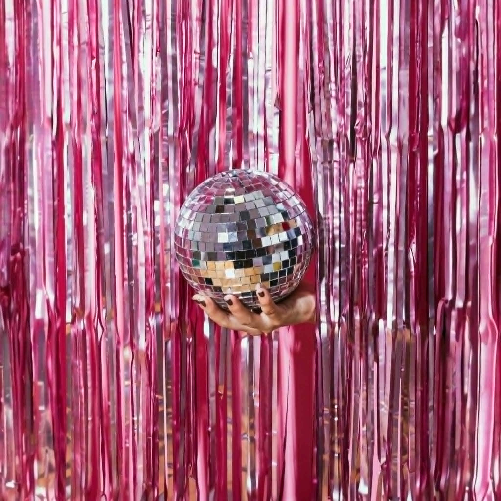 Hand holding a disco ball in front of pink tinsel curtain