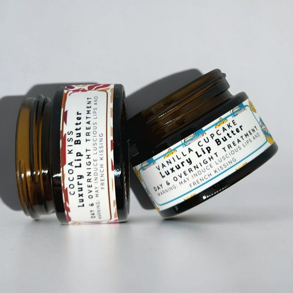 Two amber glass cosmetic jars on a light gray background. One jar is open and shows a cream product inside, labeled Cocoa Kiss Luxury Lip Treatment.