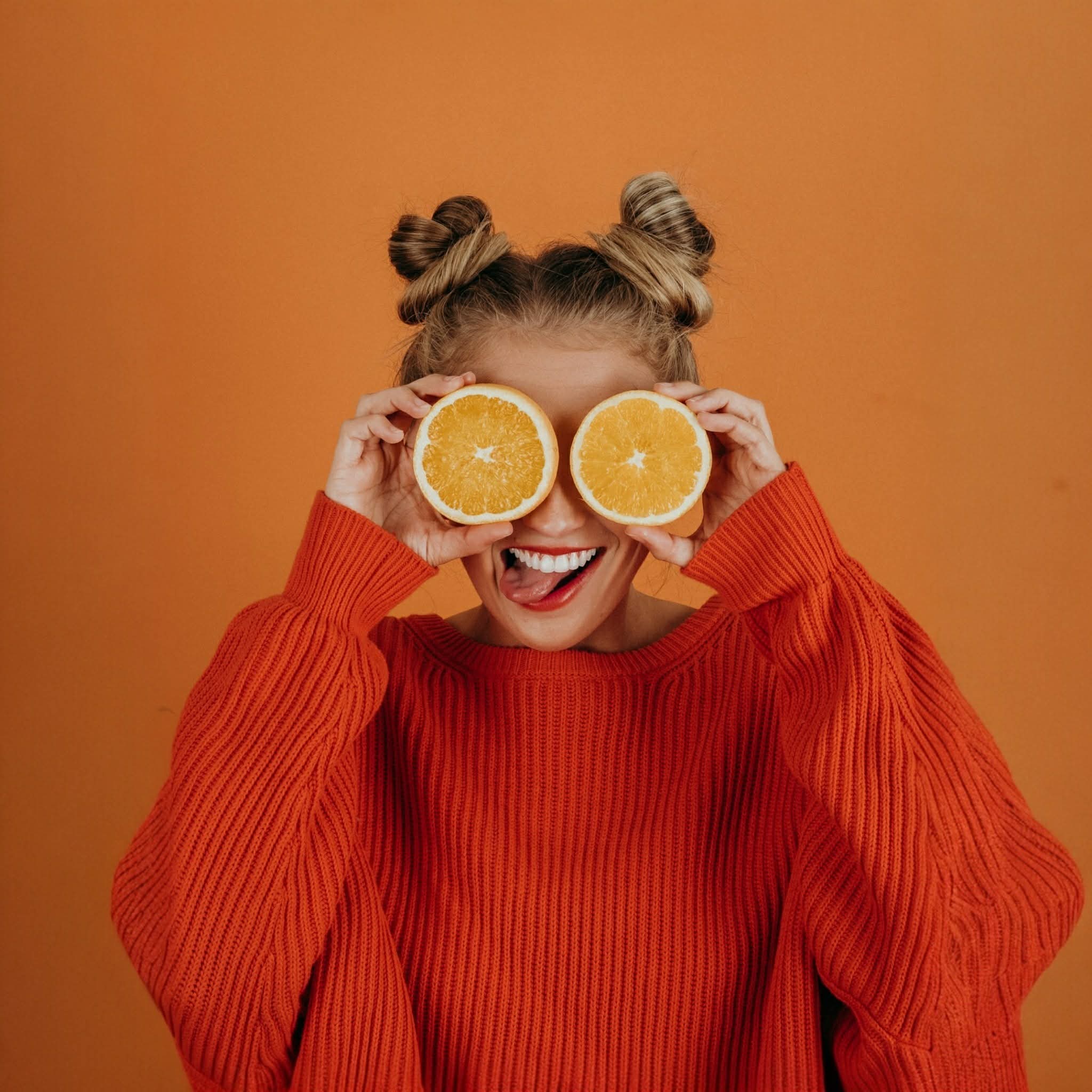 Girl posing with oranges with a orange jumper and orange background
