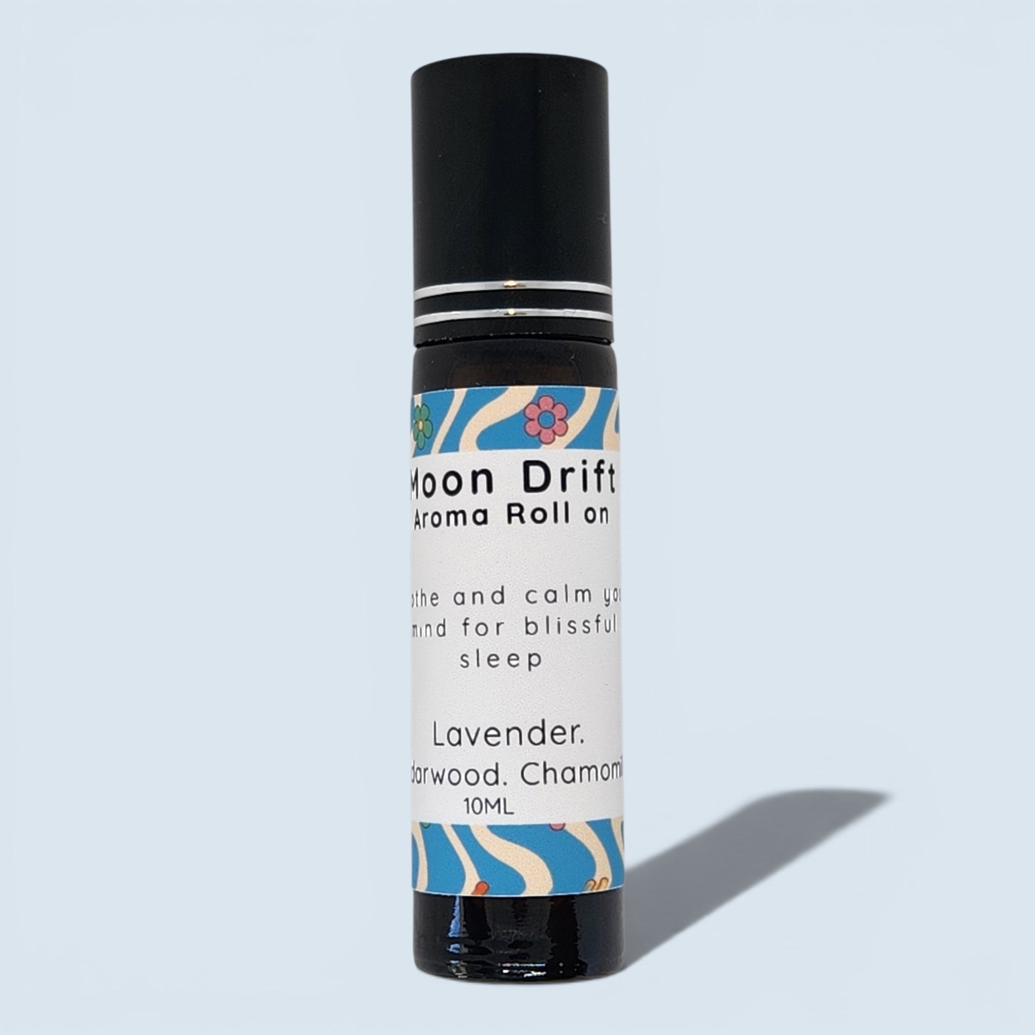 A 10ml roll-on bottle of Moon Drift Lavender aroma roll on, featuring a black cap and a white label with blue and pink floral patterns, set against a light blue background.