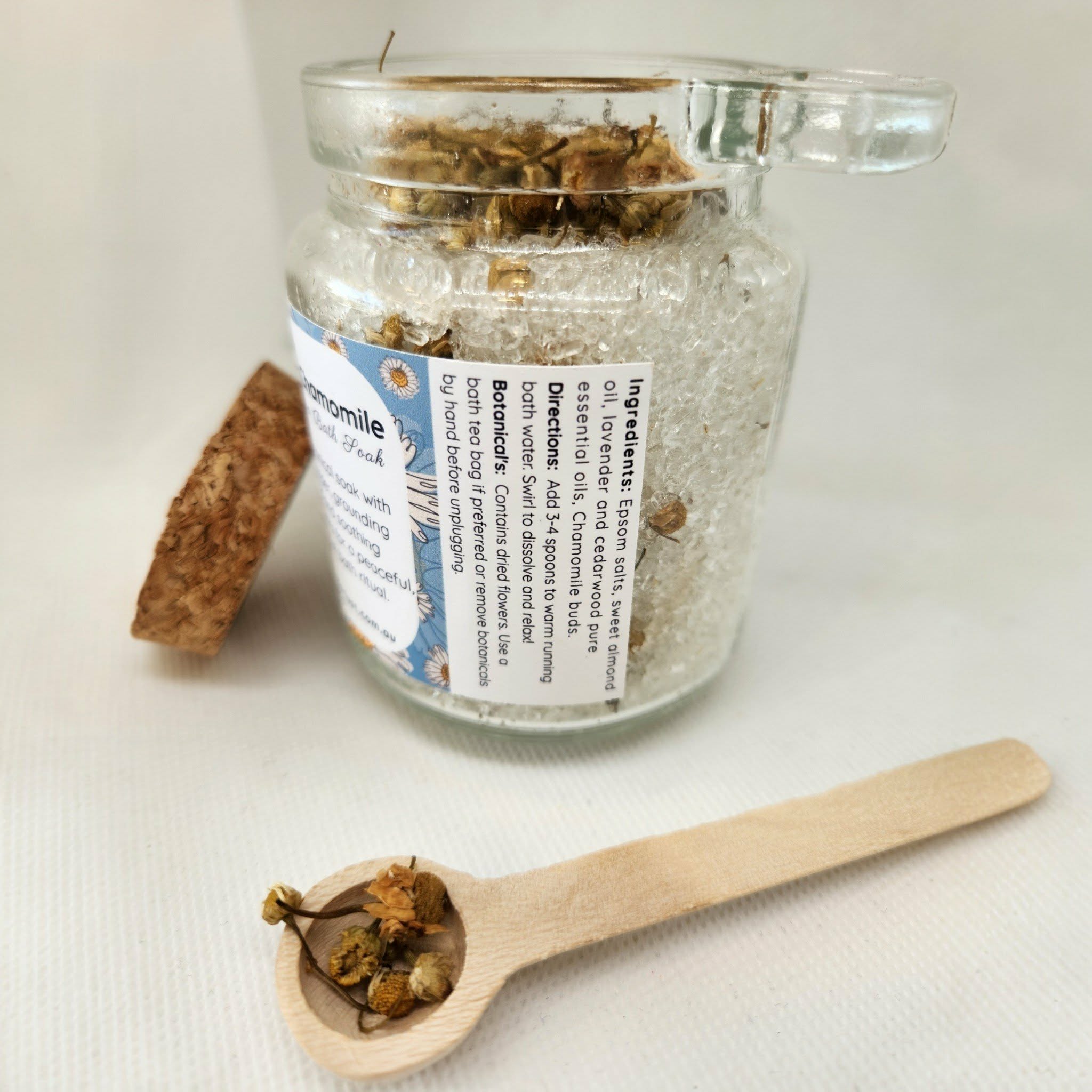 Glass jar with bath salts and a wooden spoon with dried herbs on a white background
