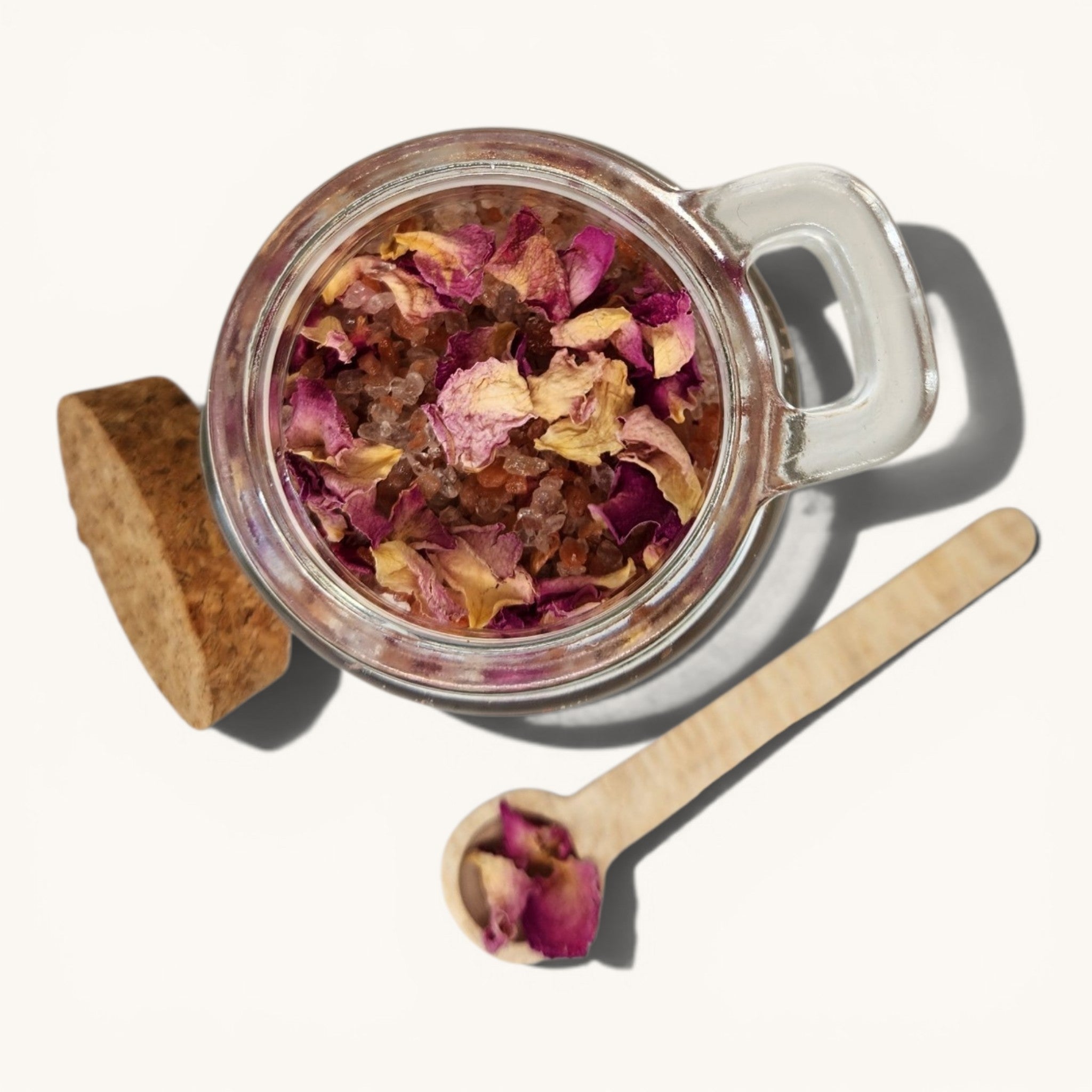 Glass jar with dried flowers, wooden spoon, and cork lid on a white background