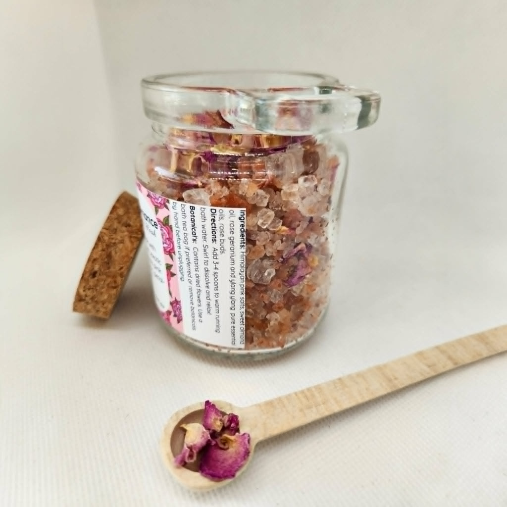 Glass jar with bath salts and a wooden spoon with dried flowers on a light background